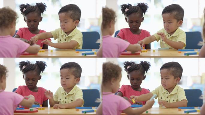 三个儿童在一张桌子旁一起搭建玩具积木。