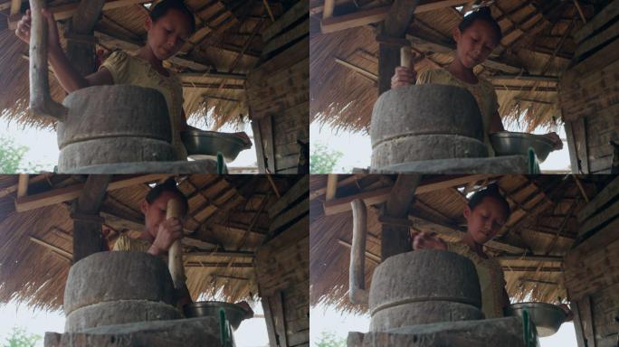 老挝农村的小女孩用石磨磨豆子 茅草屋