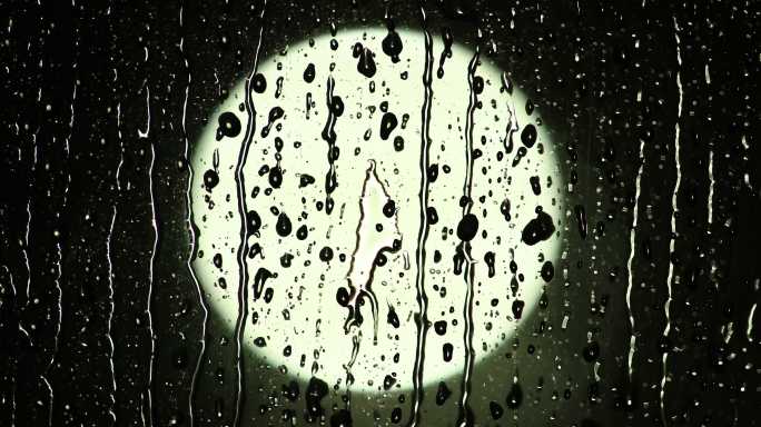 雨滴从玻璃窗上滑落，背景为散焦光。