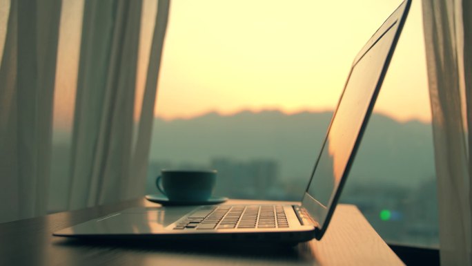 日落时，笔记本电脑放在靠窗的木桌上