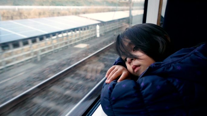 坐在火车上看窗外的小女孩。