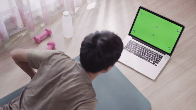 男子在家使用带绿色屏幕显示的笔记本电脑进行锻炼