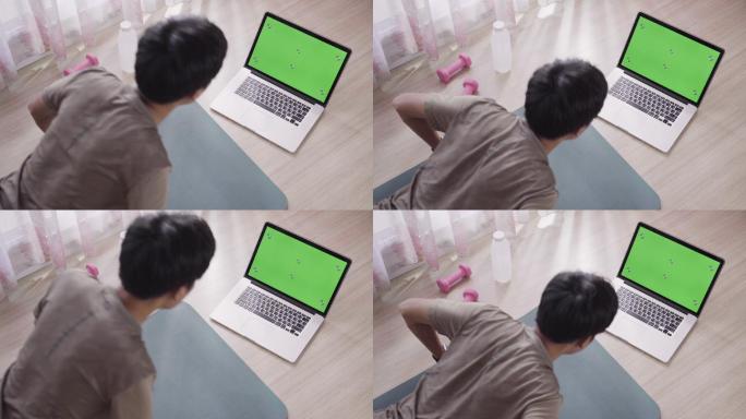 男子在家使用带绿色屏幕显示的笔记本电脑进行锻炼