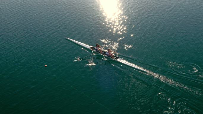 两名划艇手双桨划过阳光明媚的湖面