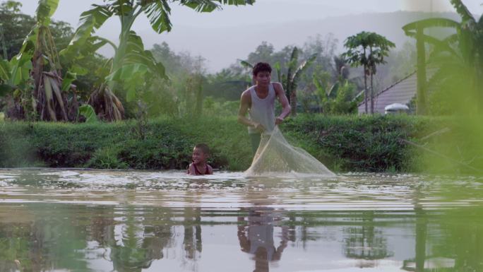 老挝乡村父子在池塘边抛渔网