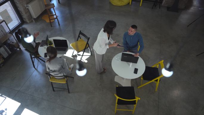 男同事坐在桌旁，女同事走近向他出示文件