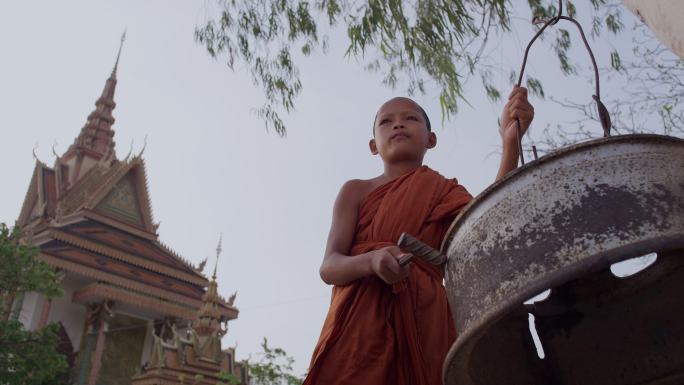 柬埔寨农村寺庙的小和尚在敲钟