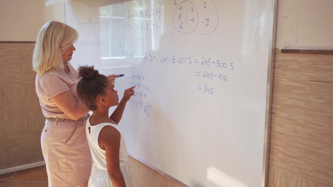 小学女生和老师在白板上做数学