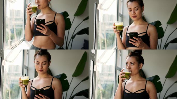 一名妇女在家使用手机时喝绿色果汁的画面