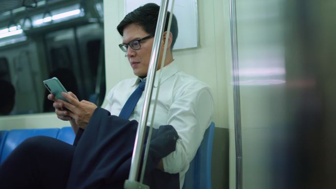 微笑的男性通勤者在地铁里用手机发短信