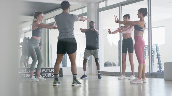 年轻男女在健身房深蹲健美操一群人围着锻炼