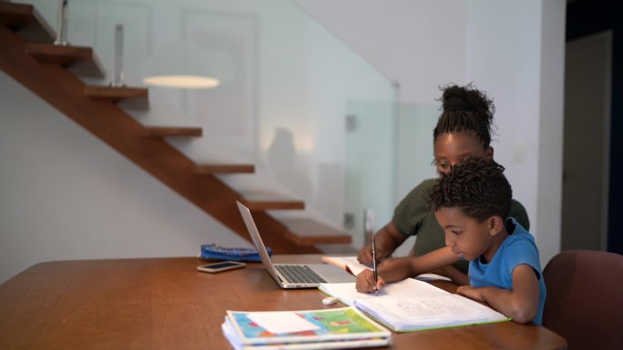 母亲帮助儿子使用笔记本电脑在家学习