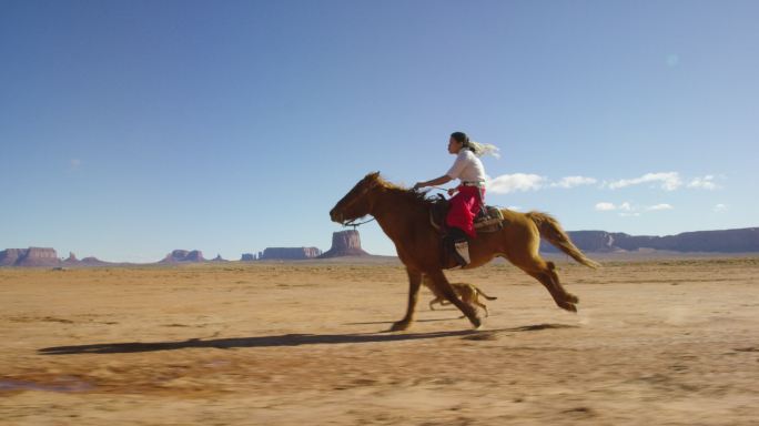 一个穿着传统纳瓦霍族服装的少女骑着马