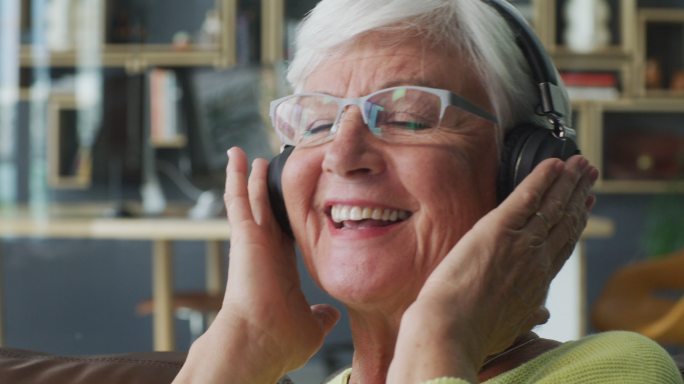一个快乐的老年妇女在家的沙发上听音乐