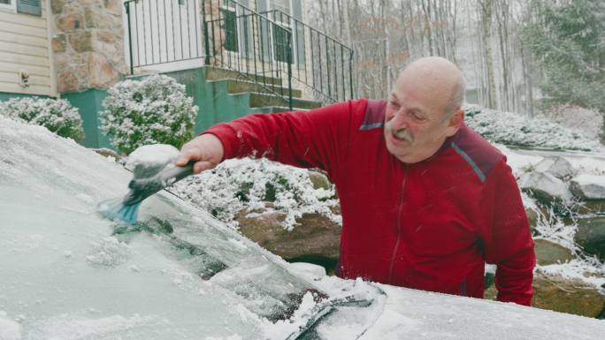 一位老人在冬天清理汽车上的积雪。