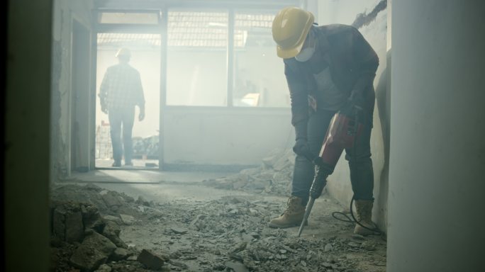 一个工人用手提钻在房子里打碎地板