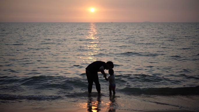 夕阳下，父子手牵着手在海滩上散步。
