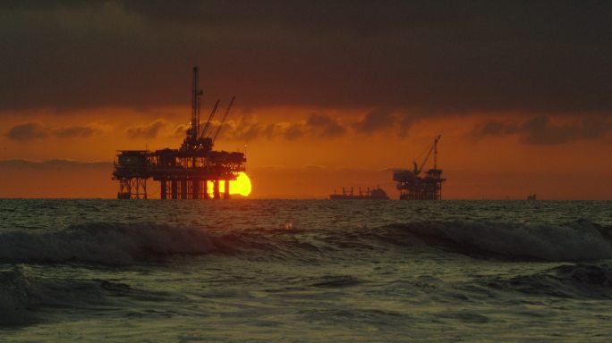 几座海上石油钻井平台的轮廓和远处一艘油轮
