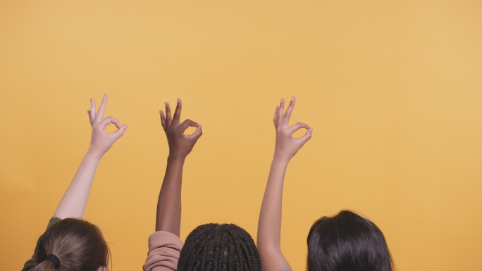 一组女孩在黄色的工作室背景下做着OK手势