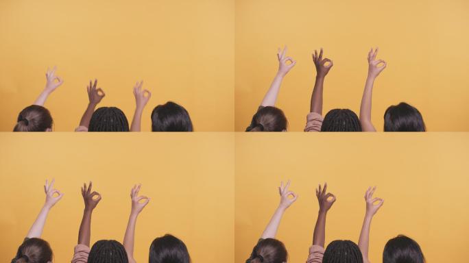 一组女孩在黄色的工作室背景下做着OK手势