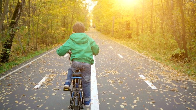 秋天在城市公园里骑蓝色自行车的男孩
