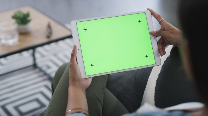 妇女在沙发上使用绿屏的平板电脑