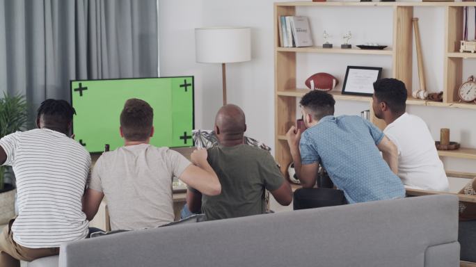 一组年轻朋友在家里的绿屏电视上观看比赛