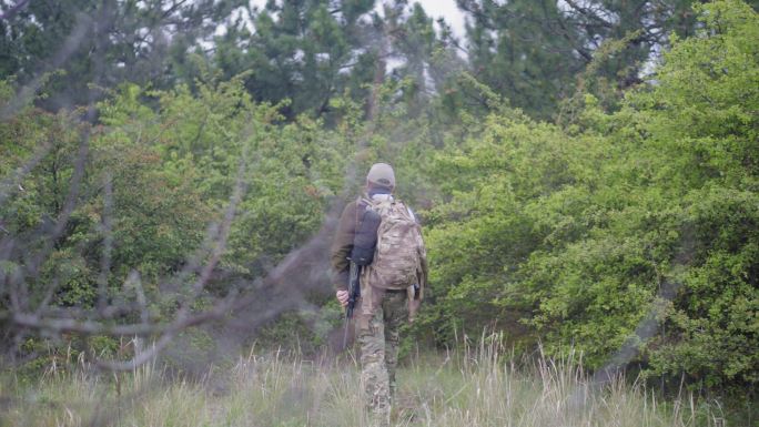 一个带着步枪和背包的猎人走进森林
