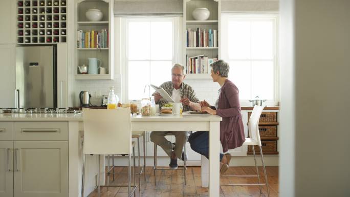 老年夫妇在家里的厨房里一起吃早餐时看报纸