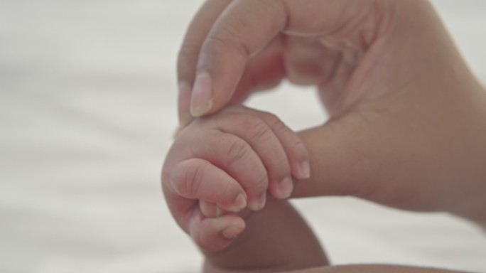 婴儿紧握着母亲的手指。