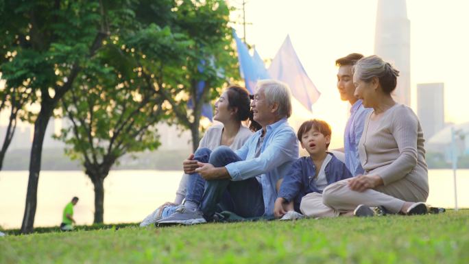 三代人家庭坐在城市公园的草地上放松