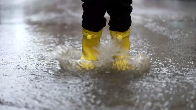穿着黄色橡胶靴的孩子在水坑里跳跃