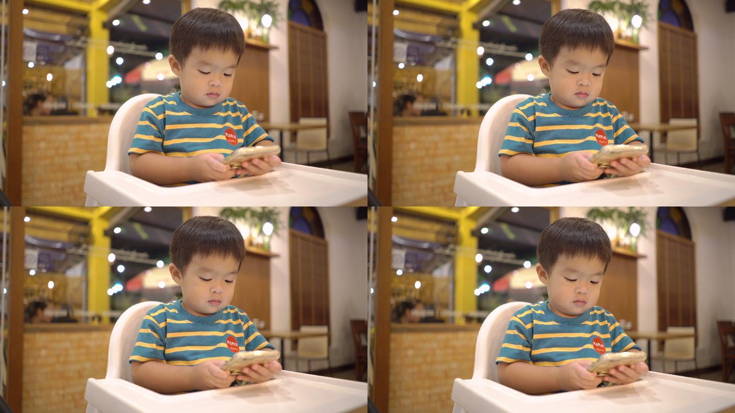 在餐厅的高脚椅上使用智能手机的幼儿