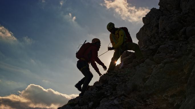登山运动员帮助绳索队队员在阳光下登上山顶