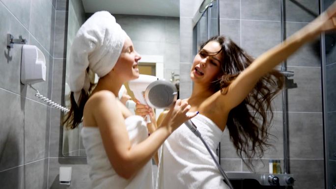 漂亮的女朋友们穿着浴巾在浴室里跳舞唱歌