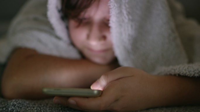 特写女孩在毯子下使用智能手机