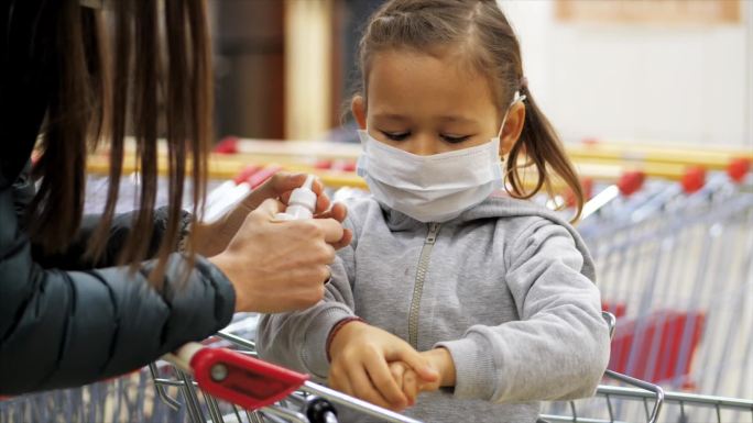 戴口罩的孩子在杂货店用消毒剂消毒双手。
