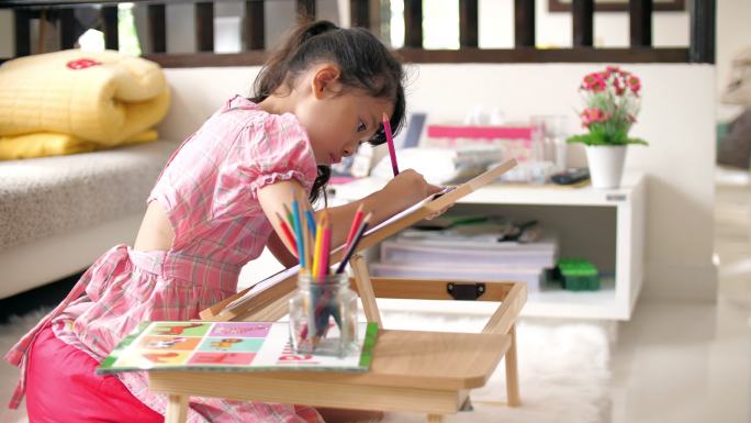 家里客厅里，一个小女孩在画册上画画写字