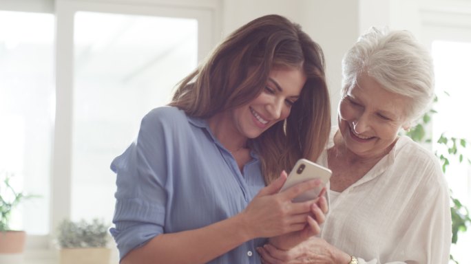 女子和她年迈的母亲在家里一起使用智能手机