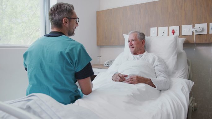 外科医生探访老年病房病床上的老年男性患者并与之握手