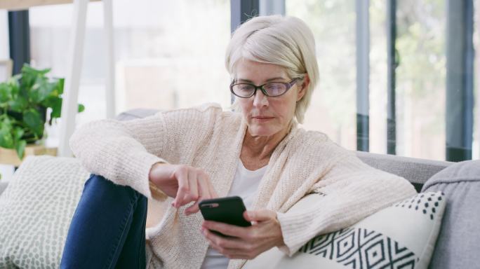 一位年长女性在家中沙发上休息时使用手机