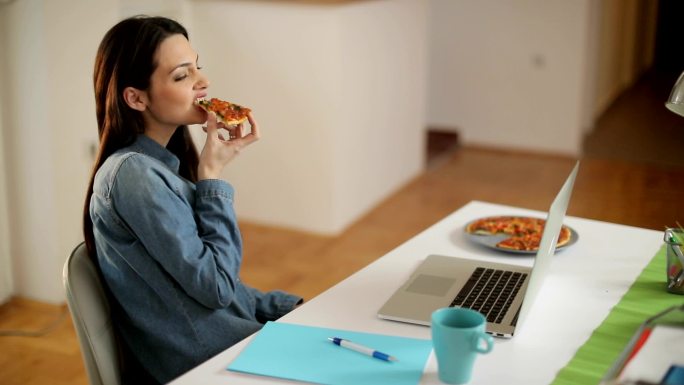 一边用笔记本电脑一边吃比萨饼的女人