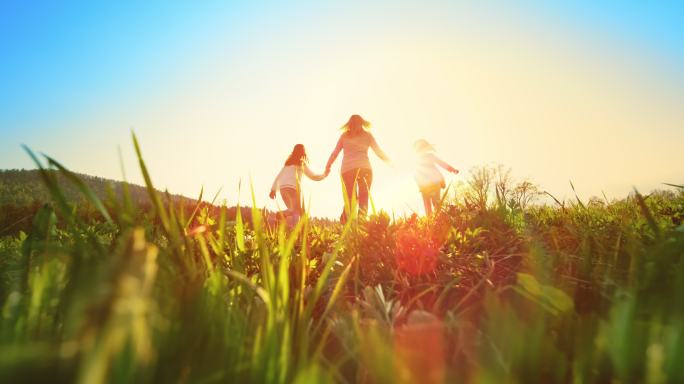 妇女牵着两个女儿的手在草地上奔跑