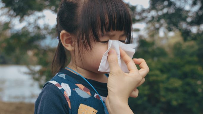 母亲手握纸巾，帮助生病的女儿擦拭和清洁鼻子