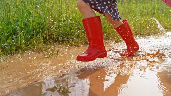 穿着红色雨靴的小女孩跑过泥泞的水坑