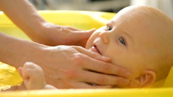 在黄色塑料浴缸中为6个月大的婴儿洗澡