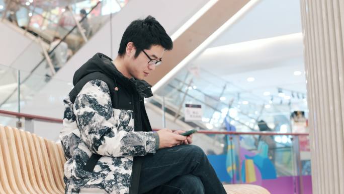 4K年轻男性在商场坐着休息玩手机特写
