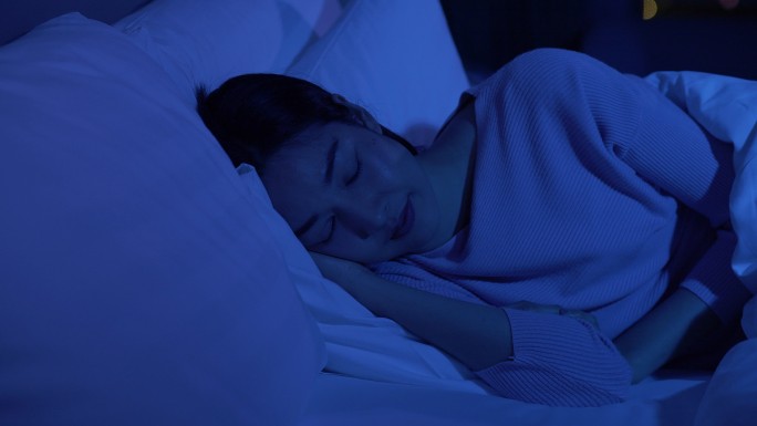 年轻女子晚上闭着眼睛睡在舒适的床上