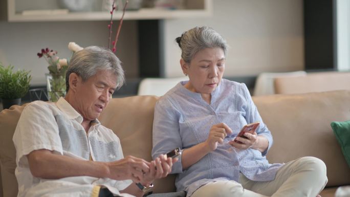 老年夫妇周末休闲时在客厅使用智能手机