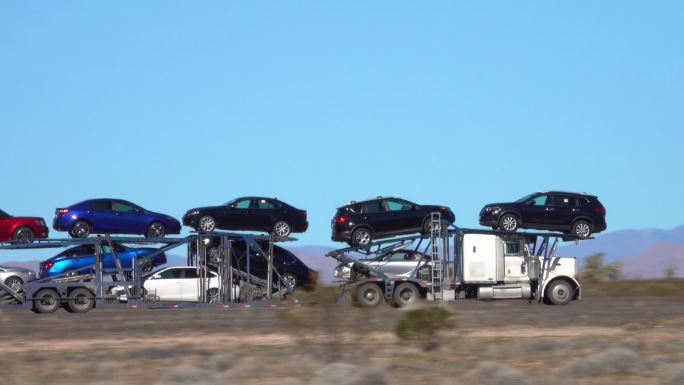 货运卡车沿着穿越沙漠的公路运送汽车。